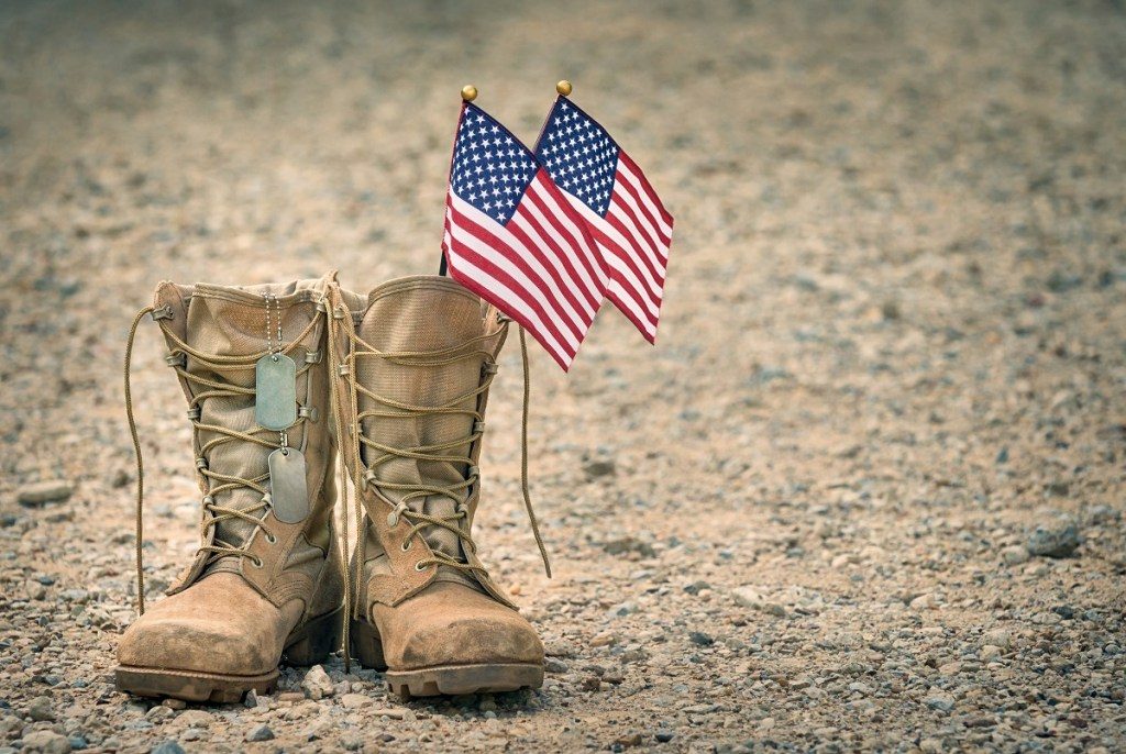 Old military combat boots with dog tags and two small American flags. Rocky gravel background with copy space. Memorial Day or Veterans day concept.